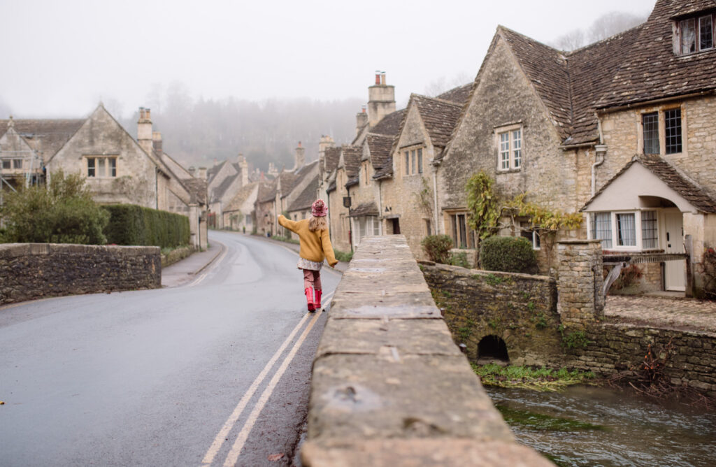A girl is walking on the bridge in a little Cotsolds village during the misty morning